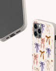 Two Bows Eco-Friendly Biodegradable Phone Cases in beige, featuring a pattern of pink, orange, and purple bows—one case displays the front of the phone, while the other shows the back design.