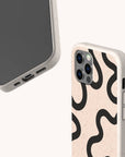 Two smartphones with Black Swirl Lines Eco-Friendly Phone Cases in beige, featuring bold black wavy abstract lines. One phone highlights the unique design near the camera, while the other reveals the front screen and bottom charging port. These cases are compostable and eco-friendly, making your choice both stylish and sustainable.