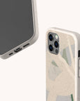 Two smartphones in beige speckled Green Abstract Lines Eco-Friendly Phone Cases with abstract green and tan designs; one shows the screen and charging port, while the other displays the camera and side buttons.