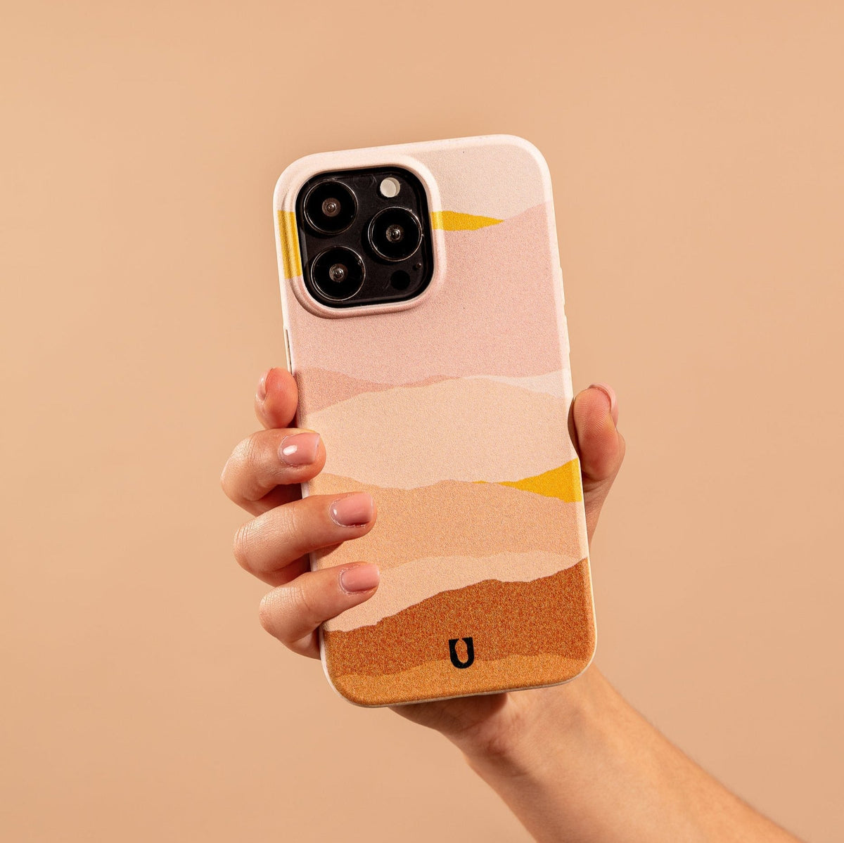 A hand holds a smartphone with the Mountains Eco-Friendly Phone Case, featuring abstract, wavy patterns in pink, peach, yellow, and orange tones against a matching beige background. This stylish and sustainable case is compatible with both iPhone and Samsung devices.
