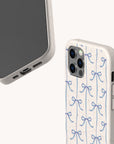 Two beige smartphone cases are featured. One, the Blue Bow Ribbons Eco-Friendly Biodegradable Phone Case, showcases a charming pattern of blue bows on the back, while the other highlights the phone’s charging port and buttons. Both cases feature a speckled texture and minimalist design, crafted from eco-friendly, biodegradable materials for sustainable style.