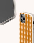 Two smartphones featuring the Terracotta Watercolour Gingham Eco-Friendly Phone Case in beige are displayed; one showcases a solid orange and white terracotta gingham pattern, while the other highlights the case’s precise port and button cutouts. Both phones rest against a simple, light background, emphasizing their sustainable design.