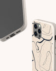 Two smartphones with beige Abstract Swirling Lines Eco-Friendly Phone Cases; one case showcases a minimalist abstract black line design with subtle swirling accents. Both cases feature precise cutouts for the camera, ports, and buttons, are compatible with iPhone and Samsung Galaxy models, and are made from eco-friendly materials. The background is off-white.