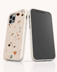 Two smartphones in beige terrazzo-patterned cases are shown: one faces forward displaying the screen, while the other reveals the Terrazzo Print Eco-Friendly Phone Case featuring multicolored specks and a small green horseshoe-shaped logo—combining unique style with sustainable phone protection.