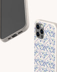Two smartphones in off-white cases are shown, with one displaying its screen and ports while the other showcases the Blue Flowers and Bow Ribbons Eco-Friendly Biodegradable Phone Case, featuring a coquette floral blue and green pattern with delicate bows. The background is plain and light-colored.