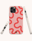 Three views of the Red and Pink Swirl Lines Eco-Friendly Phone Case on a smartphone, showcasing its light pink, speckled biodegradable material and bold wavy red lines. Compatible with both iPhone and Samsung devices, the case includes a subtle black horseshoe logo near the bottom.