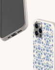 Two smartphones in speckled beige cases are pictured against an off-white background; one features the Blue Ditsy Flowers Eco-Friendly Biodegradable Phone Case, adorned with a blue and purple floral pattern, while the other showcases a plain edge with visible phone ports and buttons.