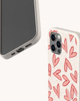 Two smartphones feature the Pink Hearts Eco-Friendly Biodegradable Phone Case in a beige hue—one displays the phone’s screen, while the other highlights the case decorated with red hand-drawn hearts. Set against a soft, solid off-white background, this elegant scene perfectly showcases sustainable accessories.