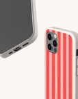 Two smartphones with beige cases—one displaying the screen, the other showing off the back with vertical red and pink stripes. Both Red and Pink Stripes Eco-Friendly Phone Cases feature precise cutouts for buttons, cameras, and ports, providing stylish protection that helps reduce your environmental footprint.