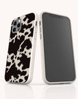 Two smartphones in white cases are showcased against a plain white background. One displays the stylish Cow Print Eco-Friendly Phone Case with its bold black and white cow pattern, while the other shows the front screen. Both cases are iPhone and Samsung compatible and made from eco-friendly materials.