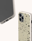 Two smartphones with beige, speckled Grunge Eco-Friendly Phone Cases are shown. One phone displays the front screen, while the other reveals the back, featuring a black paint splatter design and triple camera lenses. These sustainable cases offer a grunge-inspired style while supporting eco-friendly choices.