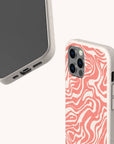 Two Pink Marble Swirl Eco-Friendly Phone Cases in beige are displayed. One case features a wavy coral pink and white abstract pattern on the back, resembling marble, while the other reveals the phone screen and ports. Both cases showcase a natural, speckled texture that highlights their eco-friendly appeal.