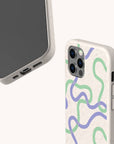 Two smartphones in Purple and Green Swirls Eco-Friendly Biodegradable Phone Cases featuring abstract blue, green, and purple wavy line designs on a beige speckled background. One phone displays the case’s back with the camera cutouts, while the other shows the screen and charging port.