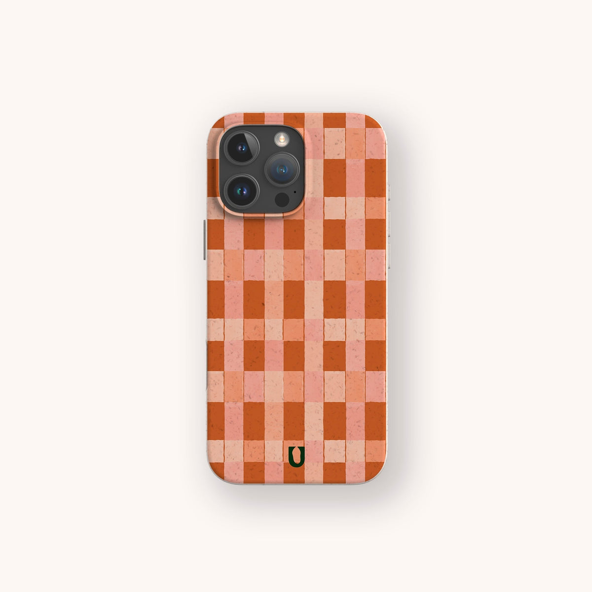 A smartphone with the Terracotta Watercolour Checker Eco-Friendly Phone Case, featuring a red and pink checkerboard pattern and a small black horseshoe-like symbol near the bottom. This compostable case is compatible with iPhone and Samsung models, combining stylish design with sustainable protection.