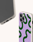 Two smartphones display the Purple and Green Swirl Eco-Friendly Biodegradable Phone Case in beige, with one showcasing a pink back accented by green swirls, photographed from both front and back angles. Both cases highlight accessible side and bottom ports and are crafted from an eco-friendly, biodegradable material for a stylish look that’s gentle on the planet.