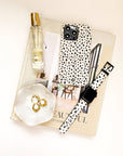 A flat lay of a book, a perfume bottle, a small dish with gold rings, and a watch is arranged on a white surface alongside the Dark Spots Eco-Friendly Phone Case for iPhone and Samsung Galaxy, featuring a minimalist black and white spotted design.