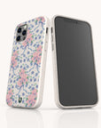 Two smartphones with white cases featuring a floral pattern of pink flowers, blue ribbons, and green leaves. One phone displays the back design of the Pink and Blue Coquette Flowers Eco-Friendly Biodegradable Phone Case, while the other shows the blank black screen. This sustainable phone case is both stylish and thoughtfully designed for eco-conscious users.