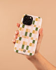 A hand holds a smartphone with the Pink and Green Watercolour Eco-Friendly Phone Case, showcasing a checkered pattern in pastel pink, peach, green, and white tones against a beige background.