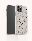 Two smartphones are pictured with the Black Terrazzo Eco-Friendly Phone Case in white, featuring a black speckled terrazzo pattern. One phone displays the screen while the other shows the back, highlighting the camera lenses and a small green logo at the bottom. This eco-conscious case combines a distinctive terrazzo design with sustainable materials for stylish protection.