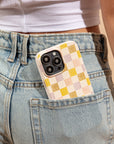 A smartphone with a pink and purple checker eco-friendly phone case peeks out of the back pocket of light blue denim jeans, worn by a person in a white cropped top.