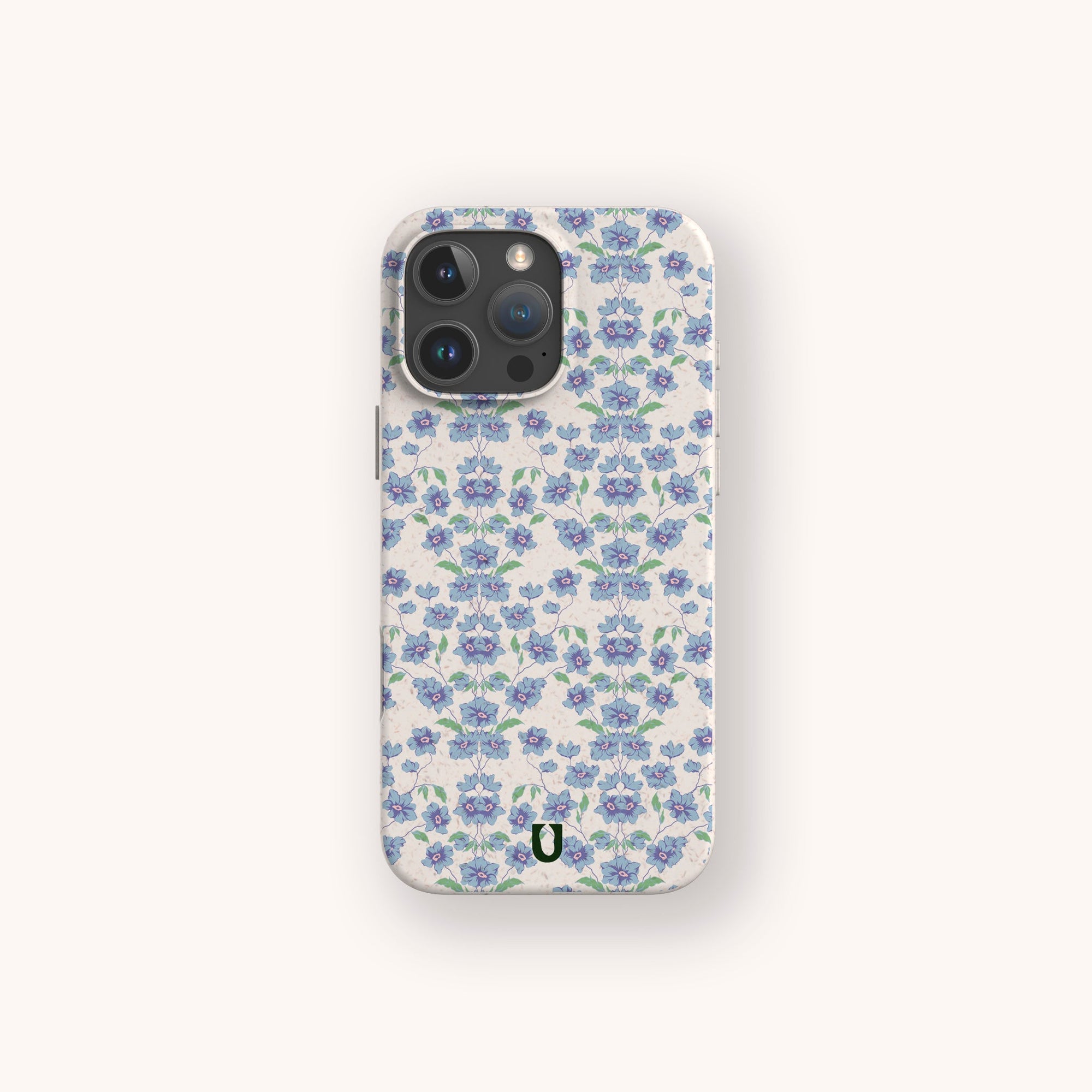 The Blue Ditsy Flowers Eco-Friendly Biodegradable Phone Case features a repeating pattern of blue and purple flowers with green leaves on a light background and a small black horseshoe logo at the bottom center.