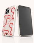 Two smartphones in Pink and Red Swirls Eco-Friendly Biodegradable Phone Cases are standing upright against a white background. One phone shows the back of the case with pink and red abstract swirled lines, highlighting the camera lenses, while the other displays its black front screen.