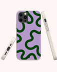 Three white smartphones are displayed at various angles, each fitted with the Purple and Green Swirl Eco-Friendly Biodegradable Phone Case. The off-white cases have a speckled texture and showcase a green wavy abstract pattern set against a purple background. The image is captured on a plain white backdrop.