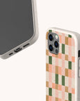 Two smartphones in speckled beige cases. One is the Pink and Green Watercolour Eco-Friendly Phone Case, featuring a pink, orange, and green checkered pattern reminiscent of a watercolour design; the other is plain. Both show camera cutouts and ports on a plain off-white background—perfect examples of eco-friendly phone case design.