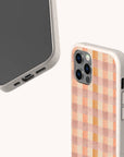 Two smartphones display the Pink and Brown Gingham Eco-Friendly Phone Case; one phone shows the screen, while the other reveals the back with a pink, orange, and beige gingham design. Both are set against a plain light beige background.